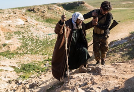 A SDF soldier helps an elderly man who fled heavy fighting in the city of Baghuz, reach a civilian collection point for suspected Isis families, on 12 February 2019