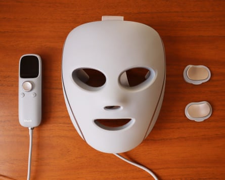 A Shark CryoGlow LED face mask lies beside its remote control and two small pads