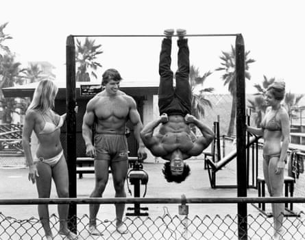 Schwarzenegger watches on as Franco Columbu hangs from a bar in the film Pumping Iron.