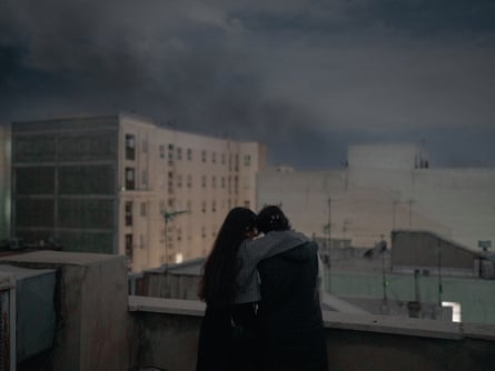 Two young women hug looking out over a city at dusk