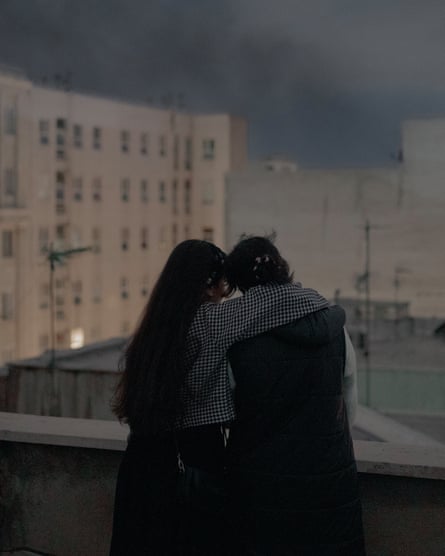Two women, backs to camera, one with her arm around the other’s shoulder, on a balcony overlooking Tehran