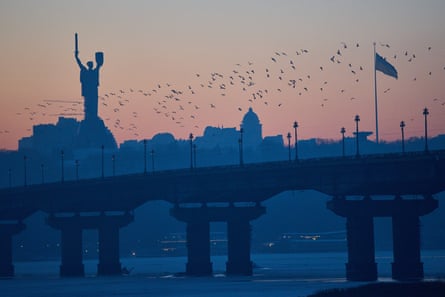 Birds flying at sunset over a bridge with the monument in the background