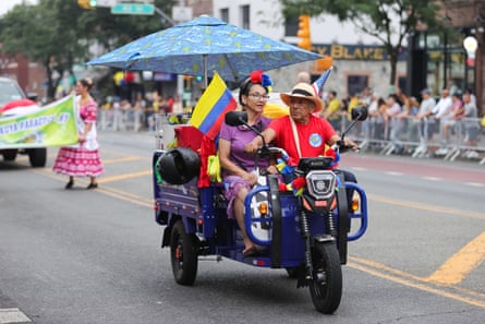 a man and a woman ride in a vehicle while holding flags during a parade