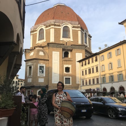She stands on a street with cars and buildings in the background