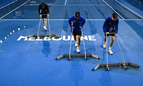 Three people clear water from an Australian Open tennis court