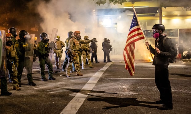 A protester holds up an American flag as federal agents make an attempt to clear a crowd in Portland, Oregon Wednesday night.