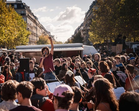 Demonstrators gather around musicians in a Parisian streetscape.