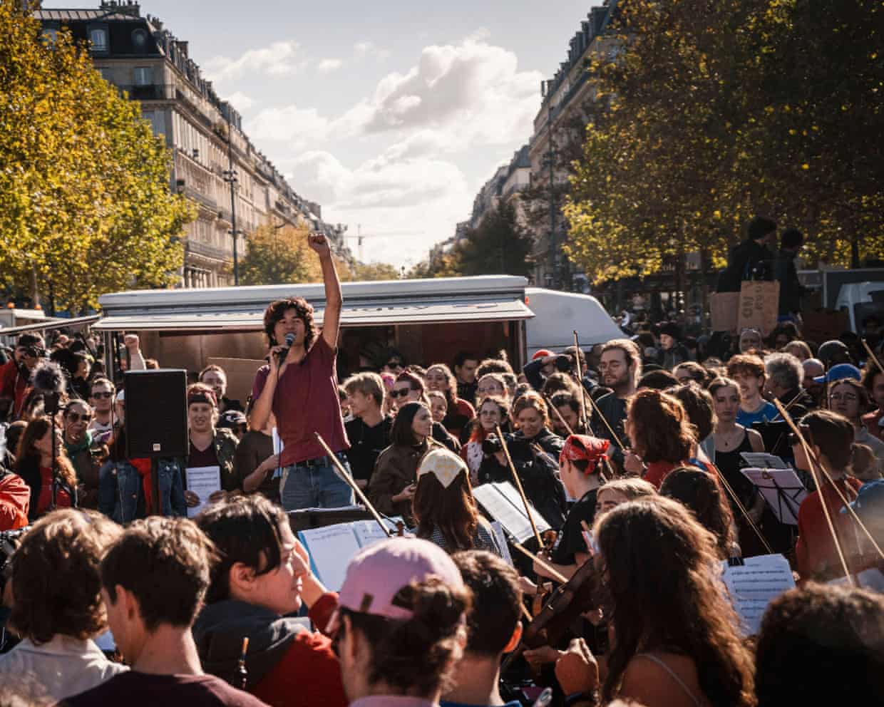 Demonstrators gather around musicians in a Parisian streetscape.
