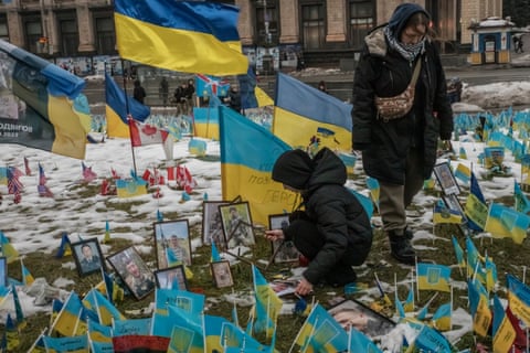 Two women fix Ukrainian flags and pictures at the memorial as snow lies on the ground