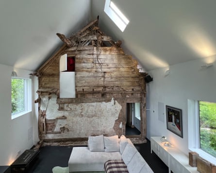 A modern living room with white walls apart from the back wall which is made of ancient timbers.