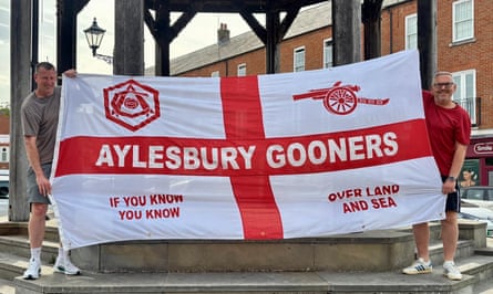 Two men hold up a white flag with a red cross, with Aylesbury Gooners written on it