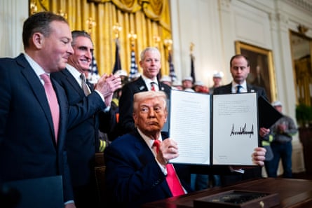 Men in suits smile while standing around a seated man holding up a signed document.