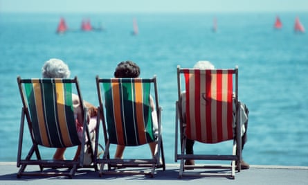 Three elderly women sit on deckchairs at the seaside