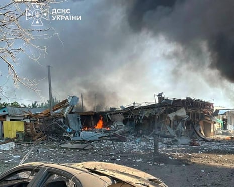 A destroyed car next to a burning building following an air attack in Pechenigy, Kharkiv region, amid the Russian invasion of Ukraine.