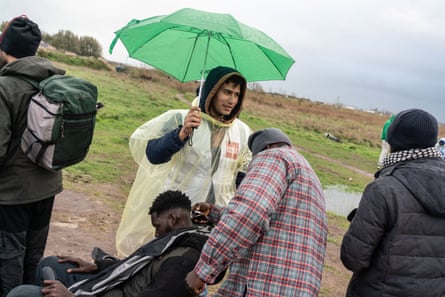 Ibrahim, 26, a Syrian student volunteering from Germany, holds an umbrella for migrants from Sudan as they shave their hair as Care4Calais, a volunteer-run refugee charity, provides hairdressing supplies for migrants.