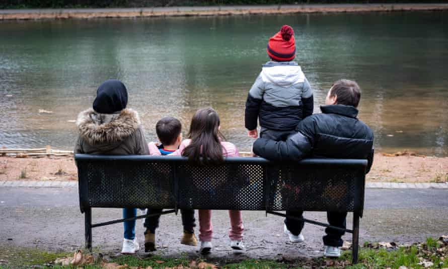 Former Foreign Office worker Ali (not his real name), sitting on a bench with his wife and children, backs to the camera