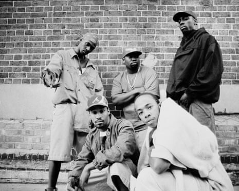 Five people posing together against a brick wall in casual streetwear