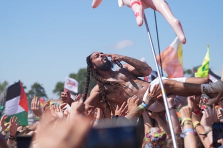 A topless Bobby Vylan crowd surfs among signs and flags, including that of Palestine.