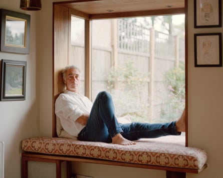 Greg Wise leans back barefoot on a cushioned window seat, gazing outside