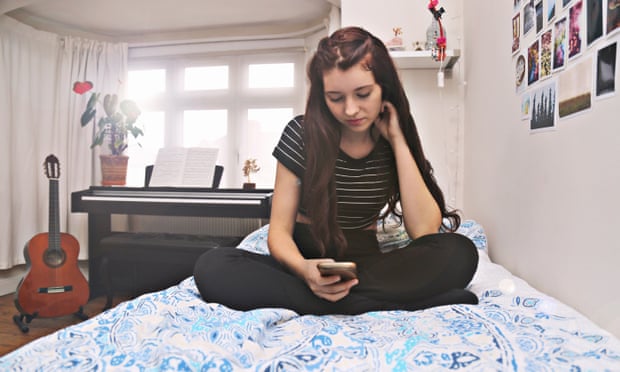 A teenage girl uses her mobile phone while sitting on her bed