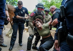 A woman crouched down, shouting out as she is handcuffed behind her back by police, some of whom are in riot gear