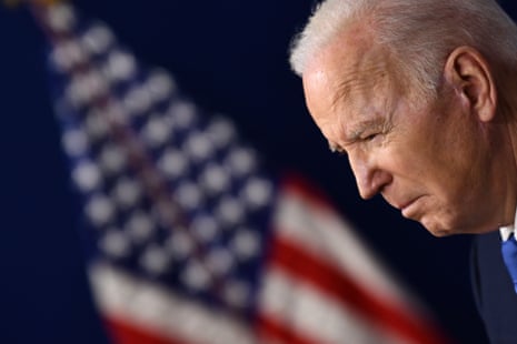 A closeup of Joe Biden's face with the American flag in the background.