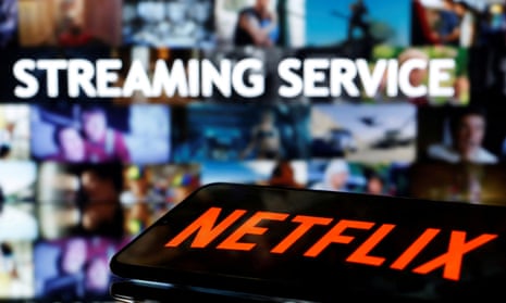 A smartphone with the Netflix logo lies in front of displayed "Streaming service" words on a screen