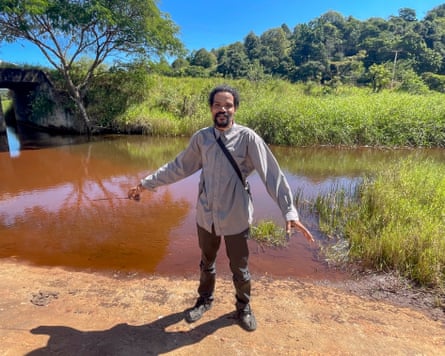 A man stands next to a red river with grassy banks