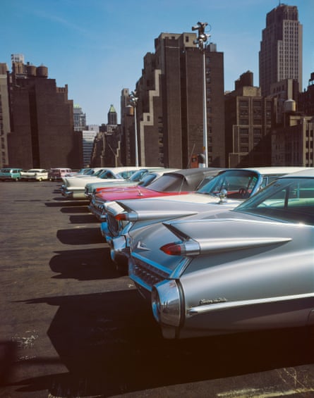 The tail fins and lights of a row of parked cars seen against a backdrop of skyscrapers