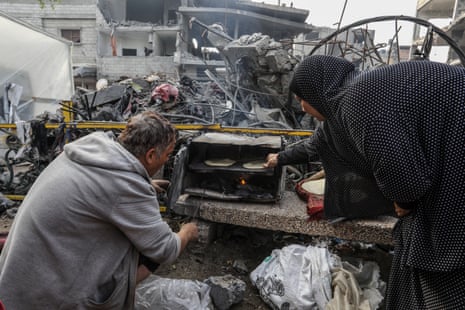 Displaced Palestinians who have moved to Gaza’s Rafah seeking refuge are seen cooking amid destruction