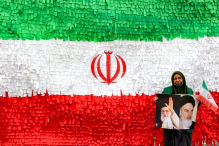 A woman holds pictures of Ayatollah Ruhollah Khomeini and Ayatollah Ali Khamenei in front of an installation depicting the Iranian flag