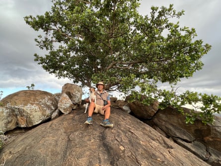 Dino Martins with his dog sitting on a large rock with a tree behind