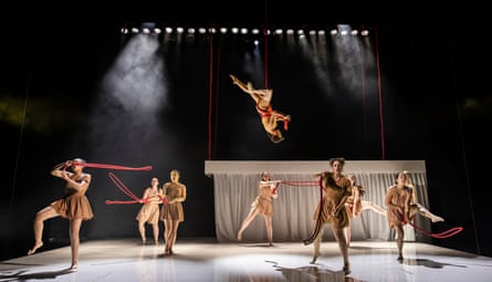 In The Penelopiad, a performer hangs upside down on ropes above dancers holding red ribbons