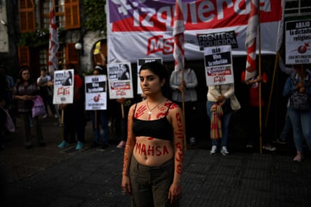 A female activist wearing a crop-top bra has 'Mahsa' and other words in Persian painted on her body, as well as red hand prints