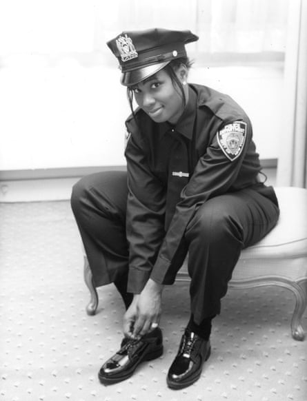 Brownlee wears her police uniform while sitting on a stool and bending down to fix her shoe.