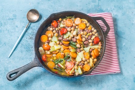 A cast iron pan full of vegetables, chickpeas and beans in stock