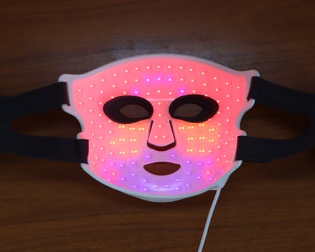 A glowing white LED face mask, the CurrentBody Series 3, lies on a wooden surface