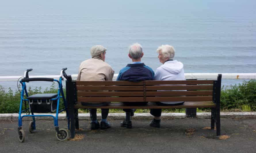 Three elderly people sitting on a bench facing the sea