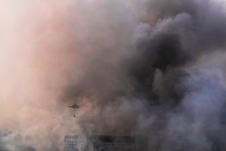 A firefighting helicopter flies as smoke rises above buildings after a drone strike in Kyiv.