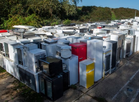 Rows of discarded fridges and freezers in white, black, red and yellow are stacked outdoors