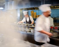 Blurred chefs in white uniforms and hats move quickly through a busy restaurant kitchen