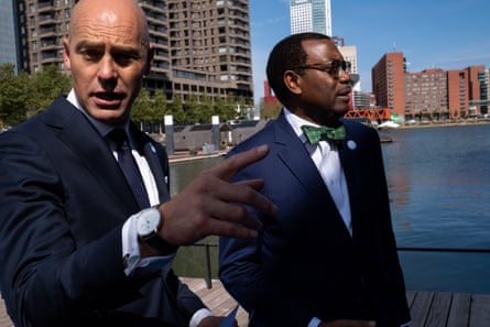 A bald European man with an bespectacled African man in a bow tie on a city waterfront