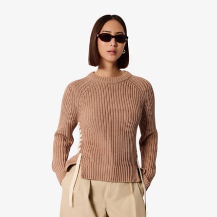 A model with short brunette hair and dark sunglasses wears the Whistles lacing detail crew jumper in taupe with sand coloured chinos.