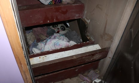 A staircase has had its step boards removed to expose a secret area filled with dirty clothing and blankets and a pillow in the shape of a panda face.