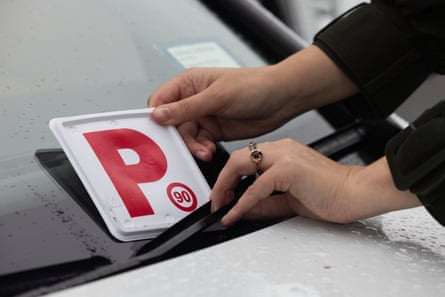 Close up of hands putting a red P-plate on a car windscreen.