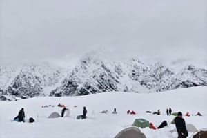 Hikers and tents in deep snow under a grey sky, with mountains in the background