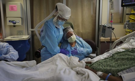 A woman is comforted by a health worker as she sits at the bedside of her husband at a Covid unit in Fullerton, California, on 31 July 2020.