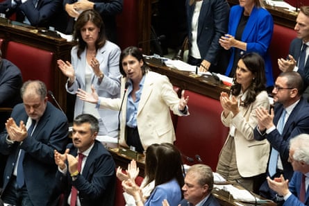 Politicans stand up from rows of red upholstered benches to applaud Elly Schlein, who stands among them with her arms spread