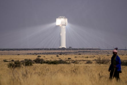 A shepherd in a field near a solar plant, which is emitting bright light