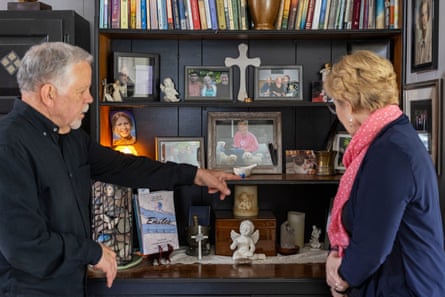 Man points to photo in cabinet with framed photos and figurines while woman looks on